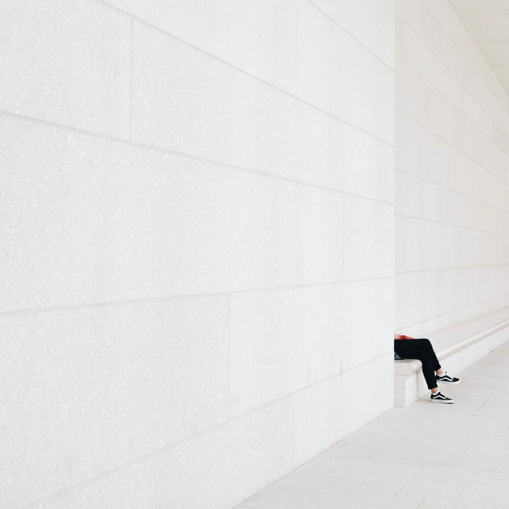 minimal white wall with person sitting on a white bench